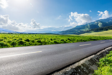 Country road and green grass with mountain scenery under blue sky
