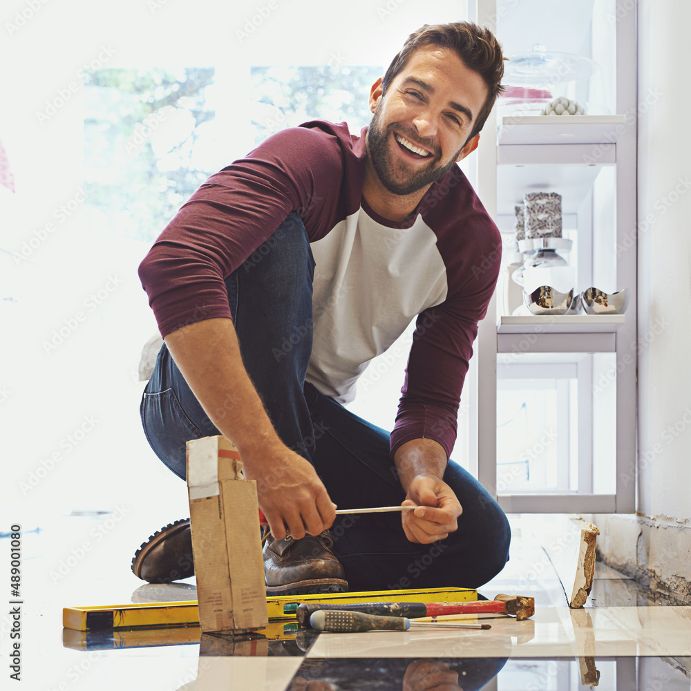 Poster decorating one tile at a time. portrait of a smiling man laying floor tiles.