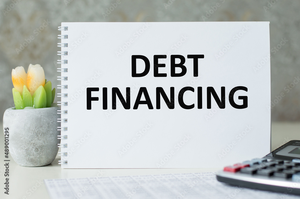 Poster the text debt financing on a notebook on the table next to the calculator and flowers in a pot