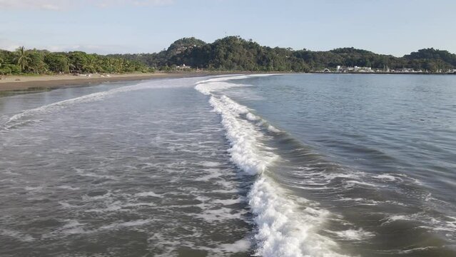 A long wave crashing ashore at the empty Quepos beach on Damas Island, Costa Rica. Low flying aerial tracking shot