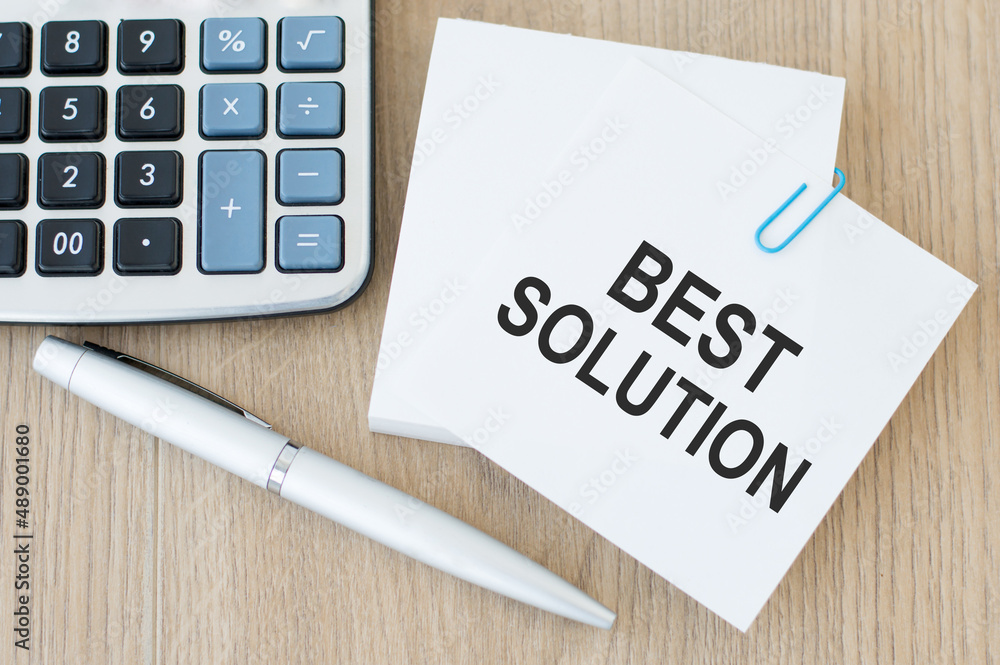 Poster the text best solution on a card on a paperclip on a wooden table next to a calculator and a pen