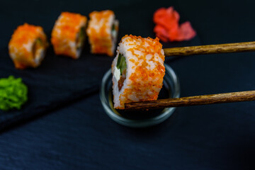 Sushi roll philadelphia with salmon, rice, cheese, cucumber, avocado and caviar on a slate board. Sushi roll in chopsticks. Japanese food