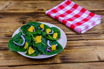 Salad with spinach leaves, pieces of orange, sesame seeds and onion in a ceramic plate