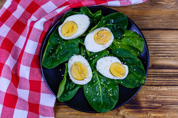 Spinach leaves and halved boiled eggs on a black plate. Top view