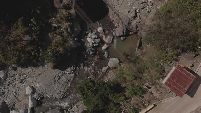 metal wire suspension bridge spanning across a rocky mountain river creek in Kabayan Benguet Philippines bird's eye view top down wide angle aerial rotating ascending