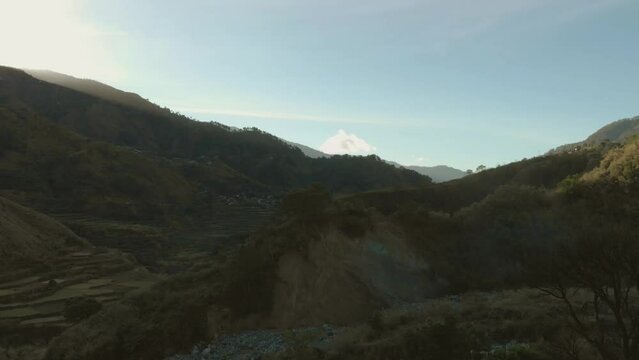 morning sun shining down on valley in mountain remote region farmland, gardens Kabayan, Benguet, Philippines aerial panning up from town to vast canyon green blue sky light flare beautiful