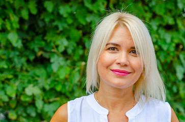 Naklejka premium Portrait of a tanned middle-aged woman. Bright makeup. Blonde. Blurred greens background.