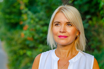Naklejka premium Portrait of a tanned middle-aged woman. Bright makeup. Blonde. Blurred greens background.