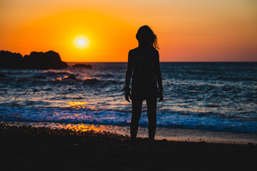 Silhouette of child in sunset on a beach. Little girl standing on sunset beach with sea in background.