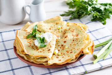 A stack of pancakes with fresh dill and onions on a white plate. Traditional Russian pancakes for Maslenitsa.