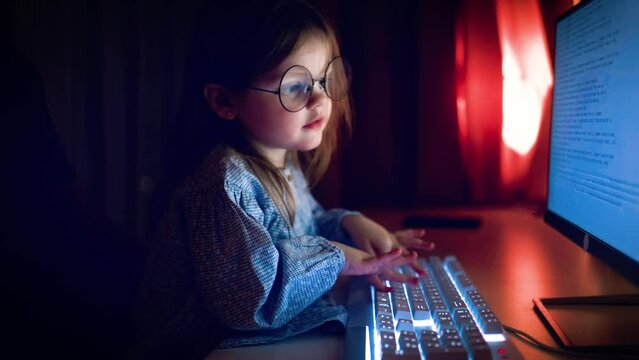 cute baby girl is typing on keybord at the computer in dark room