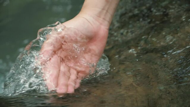 Hand touching waterfall in the green forest river or lake. Travel enjoying feel the nature and life concept in slow motion.