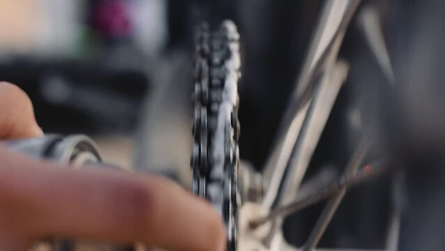 Close up of hand spraying lubrication on bike chain while rotating, in slow motion.