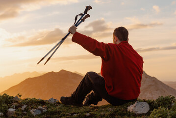 man sitting on his back on the mountain, contemplating the landscape at sunset and raising his...