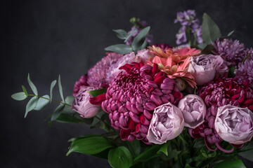 Flower arrangement of purple chrysanthemums, roses and eucalyptus branches on black background....
