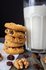 A glass of milk stands on the table next to a stack of raisins and nuts cookies