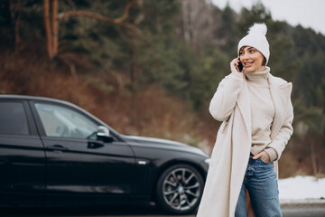 Naklejka premium Woman talking on the phone by her car on the road in winter forest