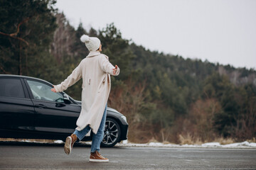 Woman walking cross the road by her car in winter forest