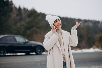 Woman talking on the phone by her car in winter forest