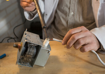 a man soldering iron solders a part from an electrical appliance. the concept of repair of...