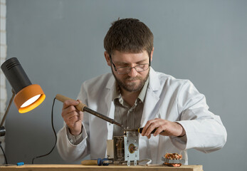a man in a white coat is sitting in his hands with a soldering iron and a spare part for an...