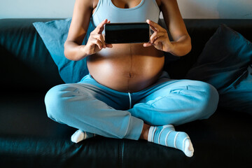 Detail of pregnant woman showing her smartphone screeen at home. Pregnancy concepts. Female holding phone in front of her belly.