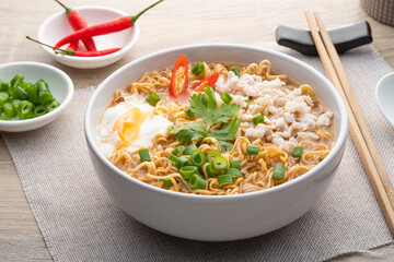 Instant noodle soup with minced pork and boiled egg in white bowl on wood table