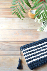 crocheted toiletry bag on wooden background with plants and candle