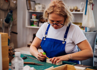 A female carpenter marks details with a pencil and cuts wood with a knife in a carpentry or...