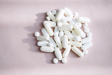 Stack of different pills, heap vitamin capsules on pastel pink background. Dietary supplement supports for health.