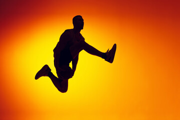 Fototapeta na wymiar Silhouette of basketball player in motion, action isolated on gradient yellow orange background in neon light. Sport, diversity, activity concepts.
