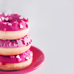 On a small red saucer are three pink delicious sweet donuts with colorful sprinkles. Beautiful dessert. Bakery products. Junk food.