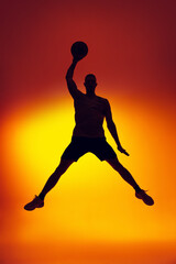 Fototapeta na wymiar Silhouette of basketball player in motion, action isolated on gradient yellow orange background in neon light. Sport, diversity, activity concepts.