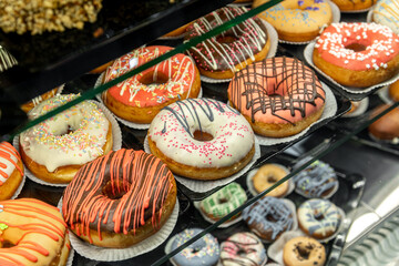 Delicious donuts decorated with different decorations displayed in cafe glass cabinet. Selective focus blured background