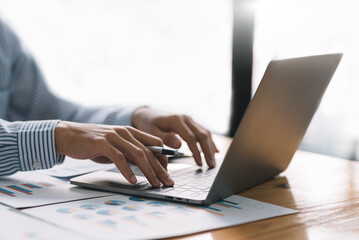 Businessman sitting using laptop computer with document on the desk in the office.