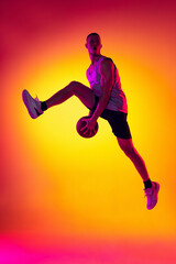 Fototapeta na wymiar Streetballer. Male basketball player, athlete jumping with ball isolated on gradient yellow orange background in neon light. Sport, diversity, activity concepts.