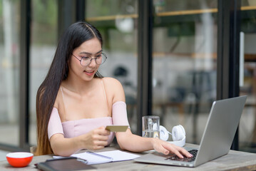 Beautiful Asian woman holding credit card and using laptop enjoying online shopping.