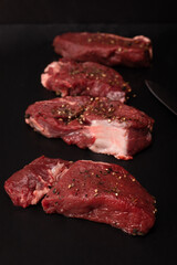 Raw beef steaks with salt and pepper on a black background, blackboard. Beef, game meat chops. Pieces of red meat.
