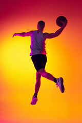Fototapeta na wymiar Streetballer. Male basketball player, athlete jumping with ball isolated on gradient yellow orange background in neon light. Sport, diversity, activity concepts.