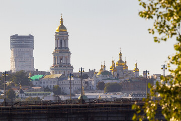 Naklejka premium Bright evening cityscape of the big city on the hill over wide river Dnipro in awesome bright sunset in Kyiv, Ukraine. View at Kyiv-Pechersk Lavra National Reserve.