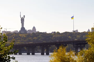 Foto op Canvas Bright evening cityscape of the big city on the hill over wide river Dnipro in awesome bright sunset in Kyiv, Ukraine. View at largest ukrainian national flag on flagpole and monument Motherland. © Sodel Vladyslav