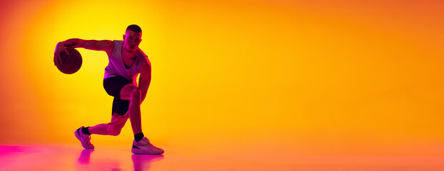Fototapeta na wymiar Flyer. Studio shot of muscled man, basketball player training with ball isolated on gradient yellow purple background in neon light. Beauty, sport, motion, activity concepts.