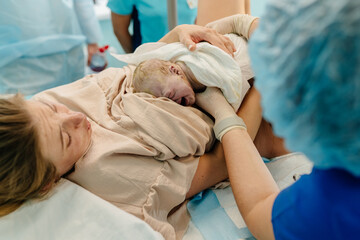 Child birth in maternity hospital. Happy mom with her newborn baby daughter after delivery. Woman giving birth. First moments of baby life after labor.