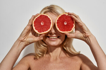 Middle aged woman covering eyes with grapefruits