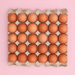 Fresh chicken eggs in cardboard box on pastel pink background. Organic food concept. Easter holidays flat lay
