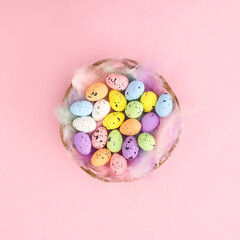 Wooden basket withfeathers and colorful Easter eggs on pastel bright pink background. Flat lay minimal spring holidays concept