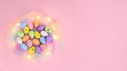 Creative Easter composition with colorful eggs on feathers on pastel pink background. Lights effect flat lay minimal arrangement. Spring holidays copy space