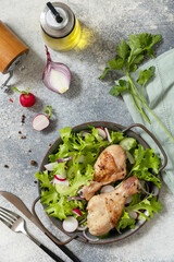 Healthy clean eating. Meat with fresh salad. Baked chicken drumsticks and a vegan salad made from a of green leaves and spring vegetables on a stone countertop. Top view flat lay.