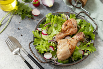 Healthy clean eating. Meat with fresh salad. Baked chicken drumsticks and a green vegan salad made from a of green leaves and spring vegetables on a stone countertop.