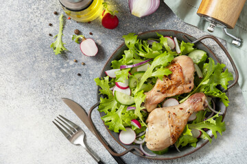 Healthy clean eating. Meat with fresh salad. Baked chicken drumsticks and a vegan salad made from a of green leaves and spring vegetables on a stone countertop. Top view flat lay. Copy space.